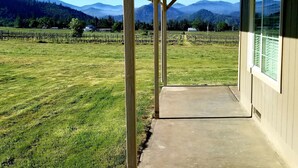 A covered porch with a view of a vineyard and mountains.