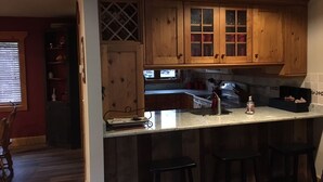 Una cocina con armarios de madera, una encimera y un lavabo. Hay tres taburetes y una ventana con persianas.