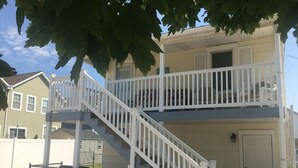 A two-story building with a white exterior, a balcony on the upper floor, and a fenced outdoor area with chairs. - 🥇PRIVATE COASTAL COTTAGE - Single Private - Central Air, Xfinity Cable, WIFI🏖 (Wildwood Crest)