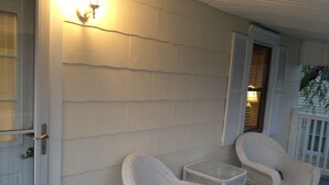 A porch with white wicker chairs and a small table, a door with a brass handle, and a wall with horizontal siding. - 🥇PRIVATE COASTAL COTTAGE - Single Private - Central Air, Xfinity Cable, WIFI🏖 (Wildwood Crest)