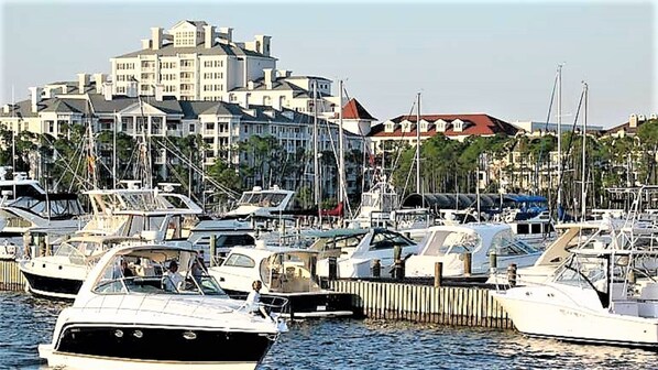 Un porto turistico con diverse imbarcazioni ormeggiate, un edificio con tetto rosso sullo sfondo e una recinzione di legno lungo la riva.
