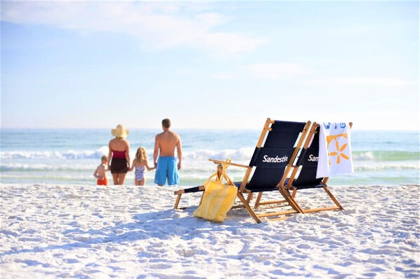 A beach scene with a family walking towards the ocean, two beach chairs labeled "Sanden" on the sand. - 2024 6 passenger GOLF CART! Lake views! 3 Minutes to BEACH! Minutes to dining (MIRAMAR BEACH)