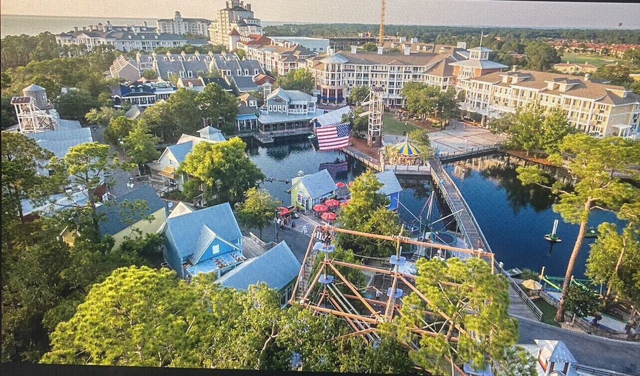 An aerial view of a theme park with various buildings, a water body, and a Ferris wheel.
