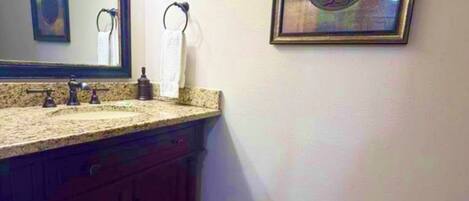 Un baño con tocador, lavabo, espejo, perchero para toallas, cuadro enmarcado y suelo de madera.