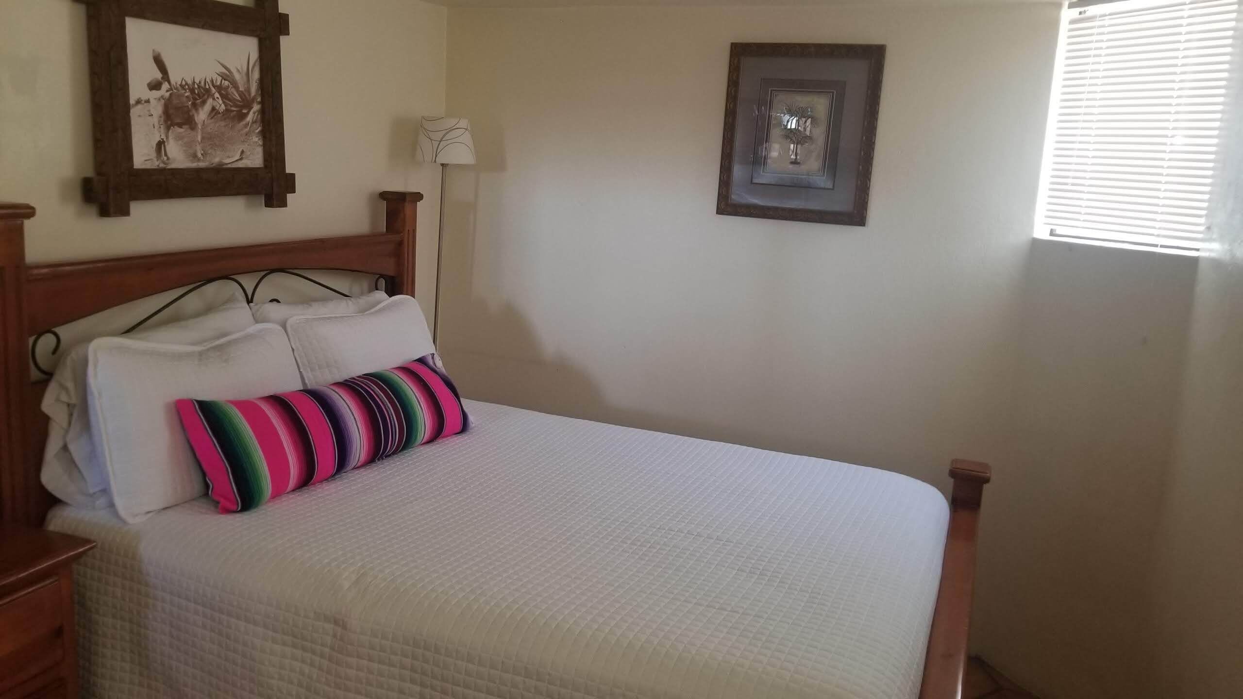 A neatly made bed with a white quilt, a colorful striped pillow, and a wooden headboard. There are two framed pictures on the wall above the bed.