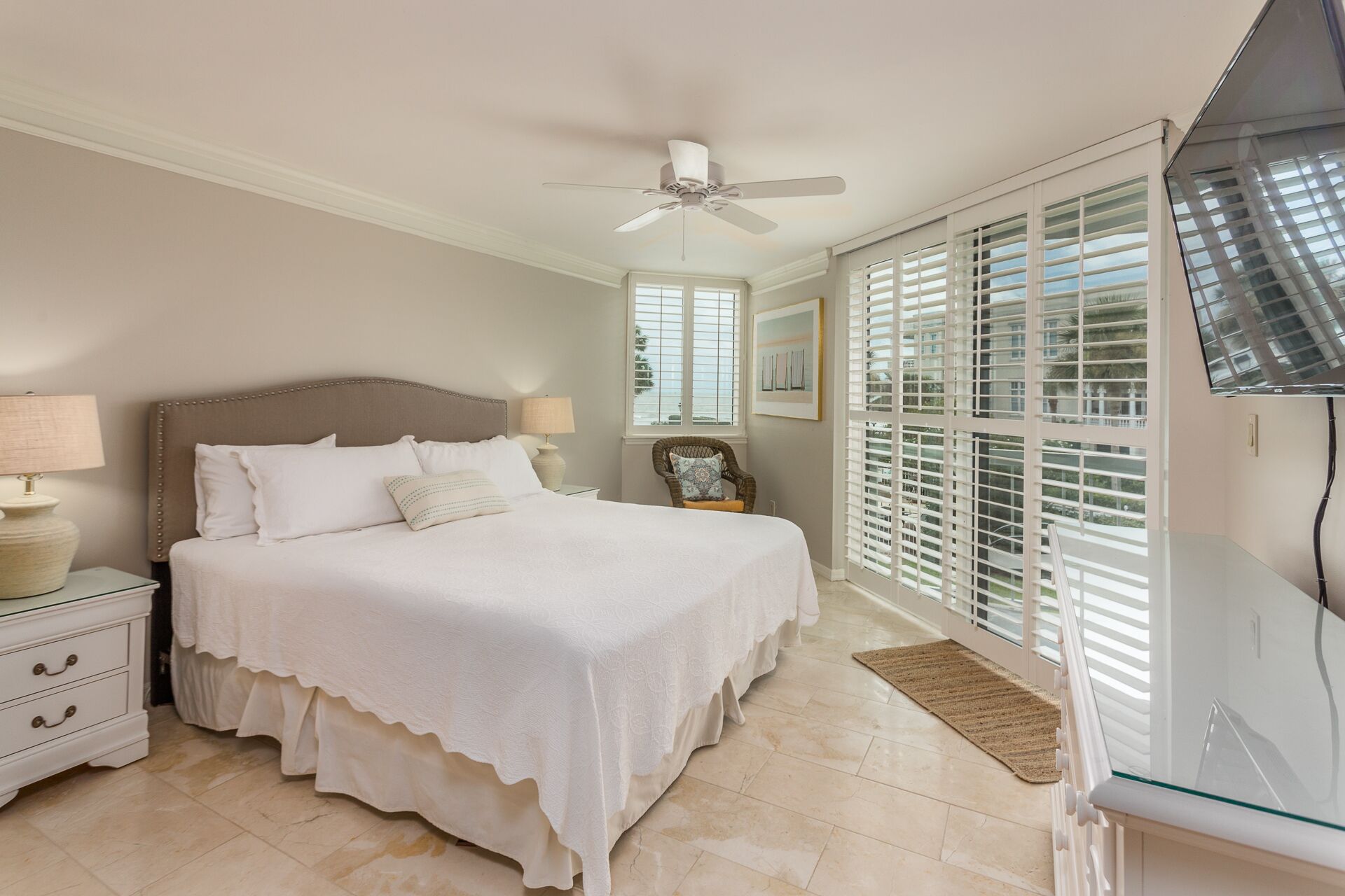 A bedroom with a bed, nightstands, a ceiling fan, and a large window with blinds.
