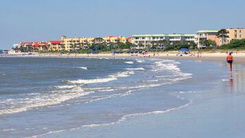 A beach scene with a row of colorful buildings, some with balconies, and a clear blue sky.