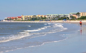 A beach scene with a row of colorful buildings, some with balconies, and a clear blue sky.