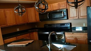A modern kitchen with wooden cabinets, a stainless steel sink, a built-in oven, and a microwave. - BEST LOCATION! Beautiful Village Home, Walk Everywhere. (Lake Placid)