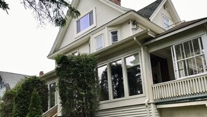 A two-story house with a large front porch, a stone retaining wall, and a garden with various plants and shrubs. - BEST LOCATION! Beautiful Village Home, Walk Everywhere. (Lake Placid)