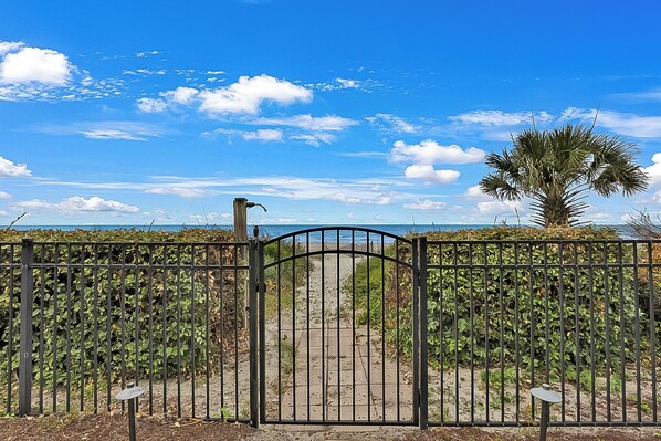 A gated entrance with a pathway leading to a beach, surrounded by dense foliage and a palm tree. - Myrtle Beach Home on the Ocean! Sun Deck! Pool! Spa! Two Master BRs! Pool Table! (Myrtle Beach)
