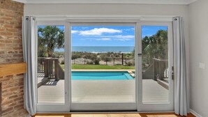 A room with a sliding glass door leading to a balcony with a pool and a view of the ocean. - Stunning Beach Home! 3 Oceanfront Masters w/ ensuite Baths! Panoramic Views!  (Myrtle Beach)