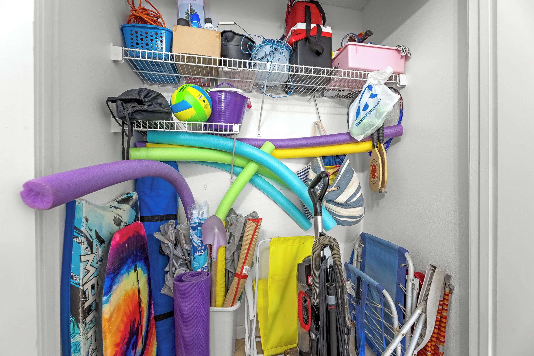 A storage area with shelves holding various items including a volleyball, cleaning supplies, and sports equipment.