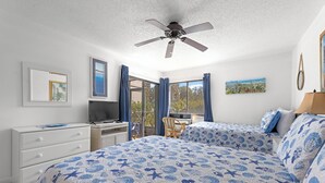Une chambre avec deux lits, un ventilateur de plafond, un bureau et une vue sur l’extérieur.