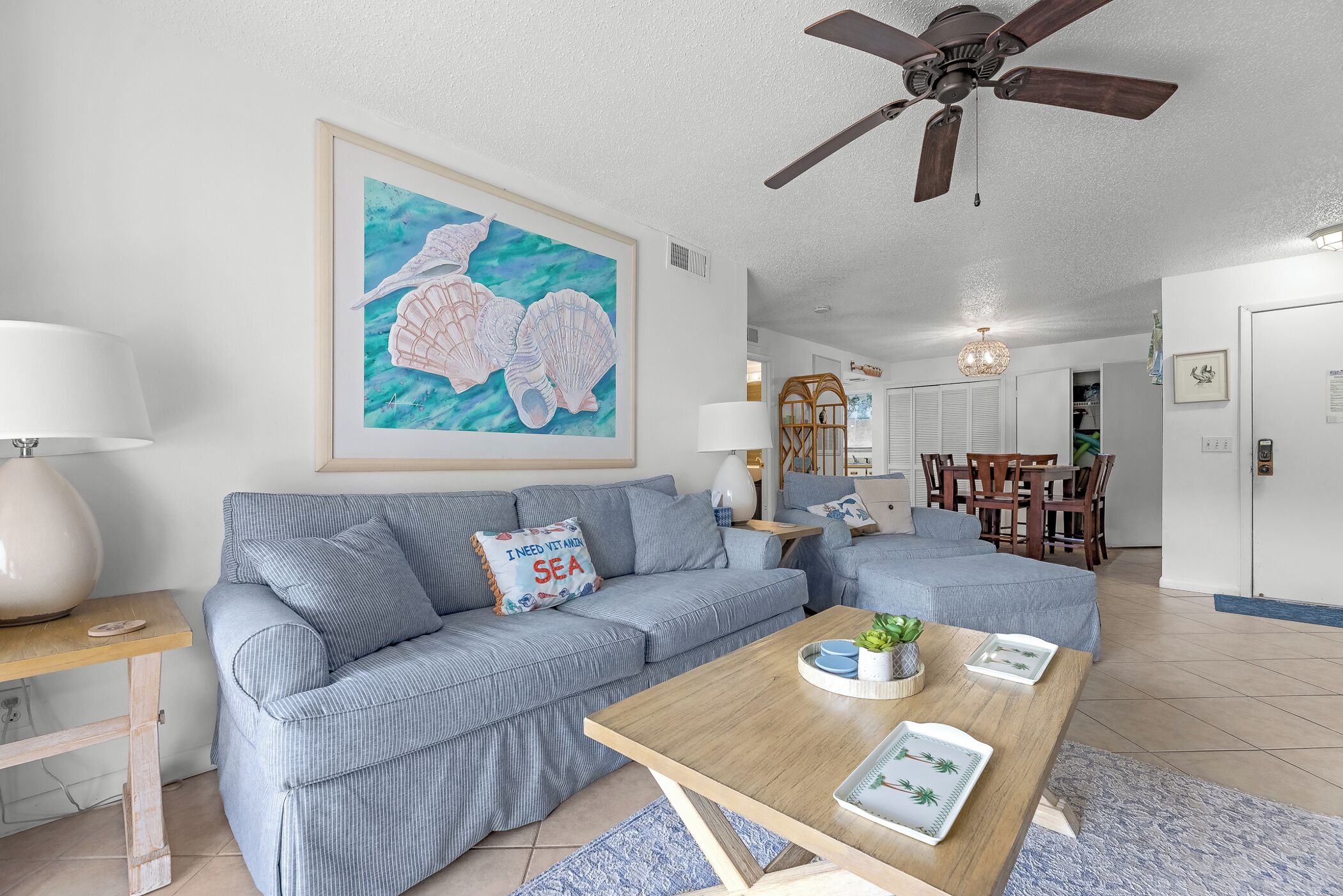 A living room with a sofa, coffee table, and a painting of seashells on the wall.