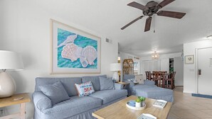 Un salon avec un canapé, une table basse et un tableau représentant des coquillages accroché au mur.