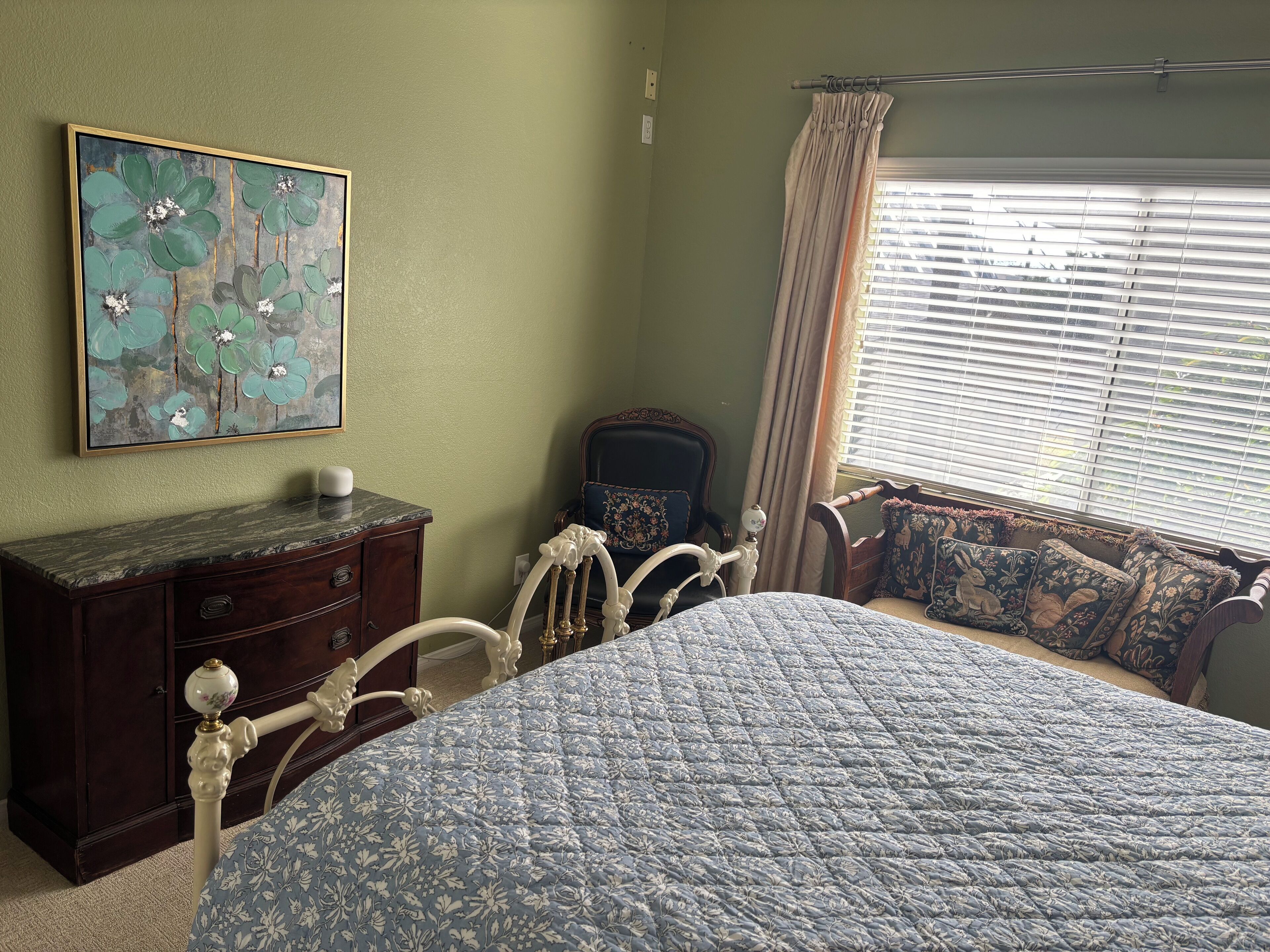 Ein Schlafzimmer mit Bett, Kommode, Stuhl, Fenster mit Jalousien und einem Gemälde an der Wand.