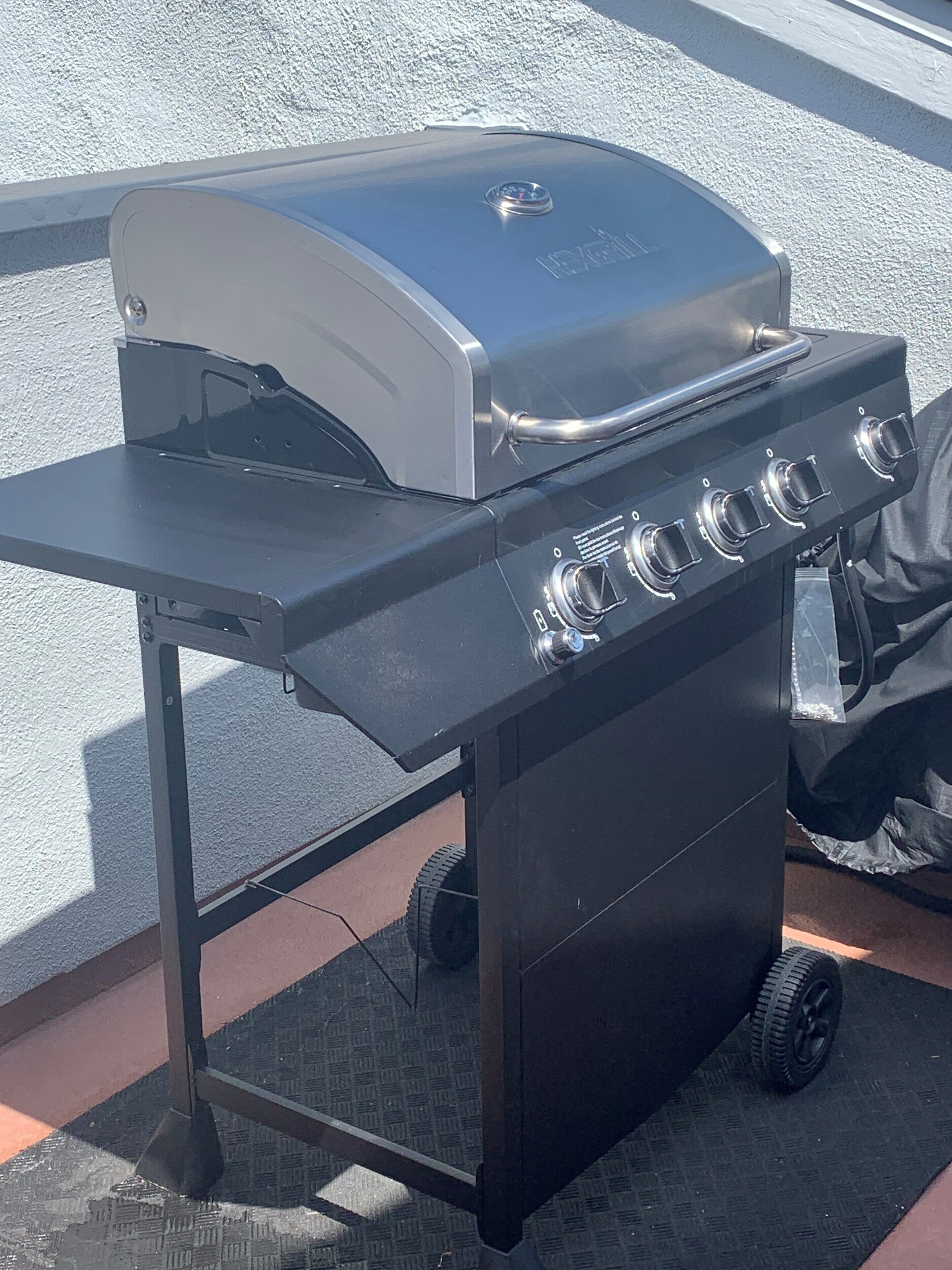 A portable grill with a lid and four burners, mounted on a wheeled cart.