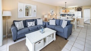 A living room with a sofa, coffee table, and a dining area with chairs and a table. - Island Princess 214-Beautiful Updated 2Bd Beachfront Condo-Free Beach Service (Fort Walton Beach)