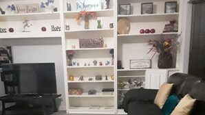 Een woonkamer met een zwarte bank, een televisie en een boekenkast vol met diverse spullen.