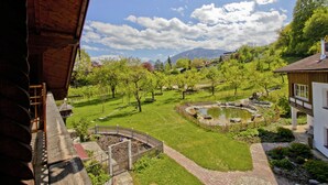 Vista de un exuberante jardín con un estanque, un puente de madera y una montaña al fondo.