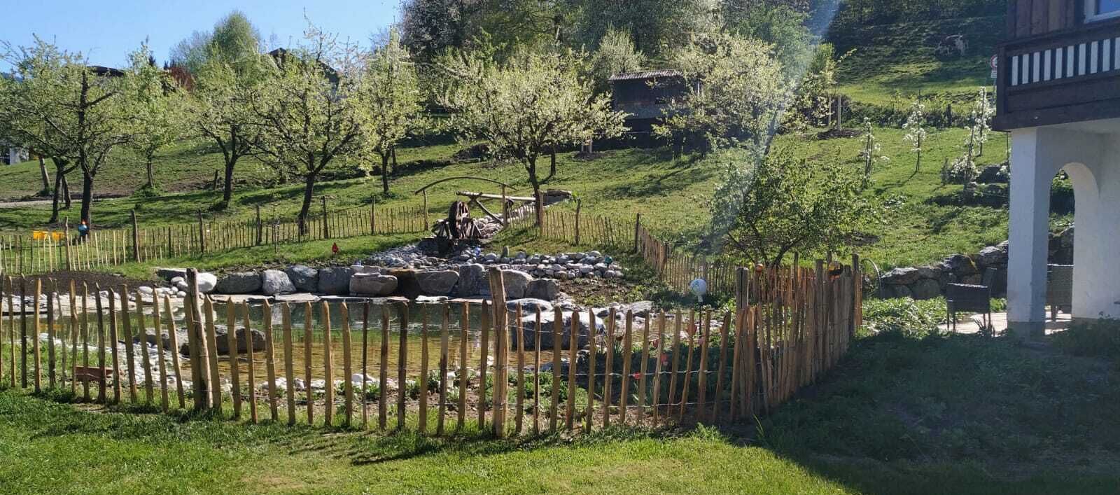 Un jardin clos, agrémenté d’un petit étang, entouré d’arbres et d’une construction en pierre.