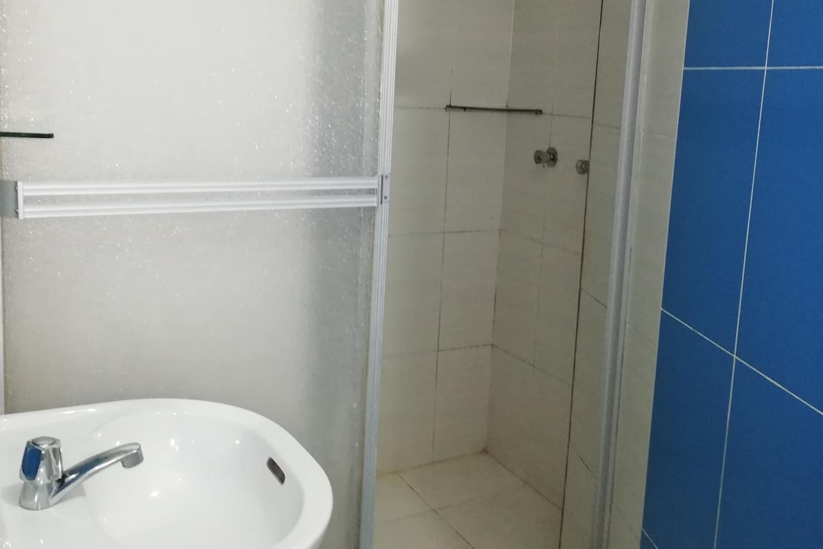 Um banheiro com pia branca, box de chuveiro em vidro e paredes azulejadas em tons de azul.