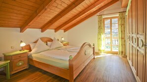 Ein Schlafzimmer mit Holzboden, einem Bett mit weißer Bettwäsche, einem Nachttisch mit Lampe und einem Fenster mit Vorhängen.