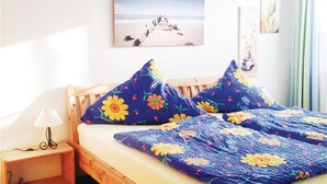 Een slaapkamer met een houten bed, bloemenbeddengoed, een bedlampje en een schilderij met een strandthema aan de wand.