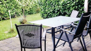 Een terras buiten met een tafel en stoelen, omgeven door een haag.