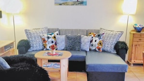 Een woonkamer met een grijze bank, gekleurde kussens, een klein houten tafeltje en een lamp.