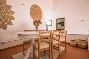 Un comedor con una mesa redonda, sillas de madera, un florero con flores y un tapiz tejido en la pared.