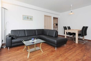 Un salon moderne avec un canapé en cuir noir, une table basse en verre et un coin repas comprenant une table en bois et des chaises noires.