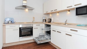 A modern kitchen with white cabinetry, stainless steel appliances, and a built-in dishwasher. - Stader Sand - House Lighthouse (Esens)