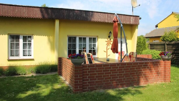 A yellow house with a brick patio, a satellite dish, and a garden with flowers and plants. - Vacation cottage Bley, Germany (Ahrenshoop)