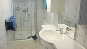 A bathroom with a glass-enclosed shower, a white sink with chrome fixtures, and a towel rack with blue towels. - Vacation cottage Bley, Germany (Ahrenshoop)