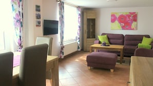 A living room with a sofa set, a television, and a dining area with chairs and a table. - Vacation cottage Bley, Germany (Ahrenshoop)