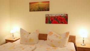 A double bed with floral bedding, two bedside lamps, and two wall-mounted paintings of poppies. - Vacation cottage Bley, Germany (Ahrenshoop)