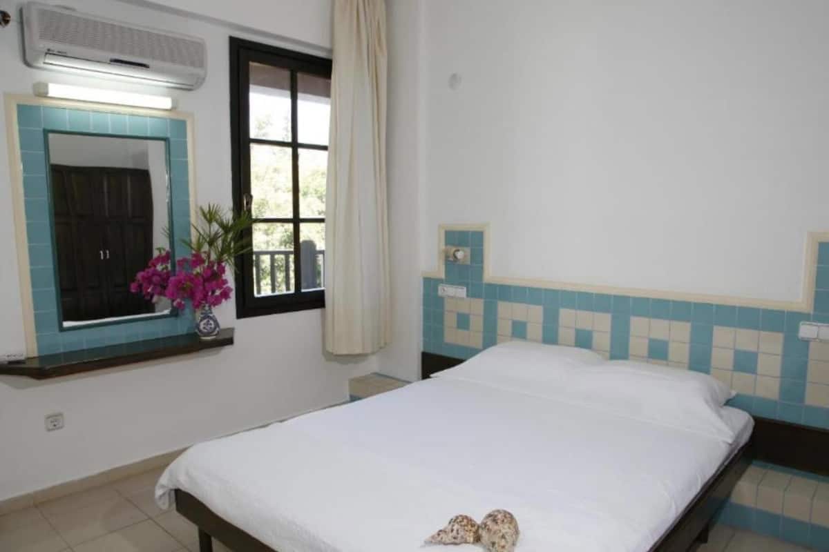 A bedroom with a bed, a window with curtains, a wall-mounted air conditioner, and a small potted plant.