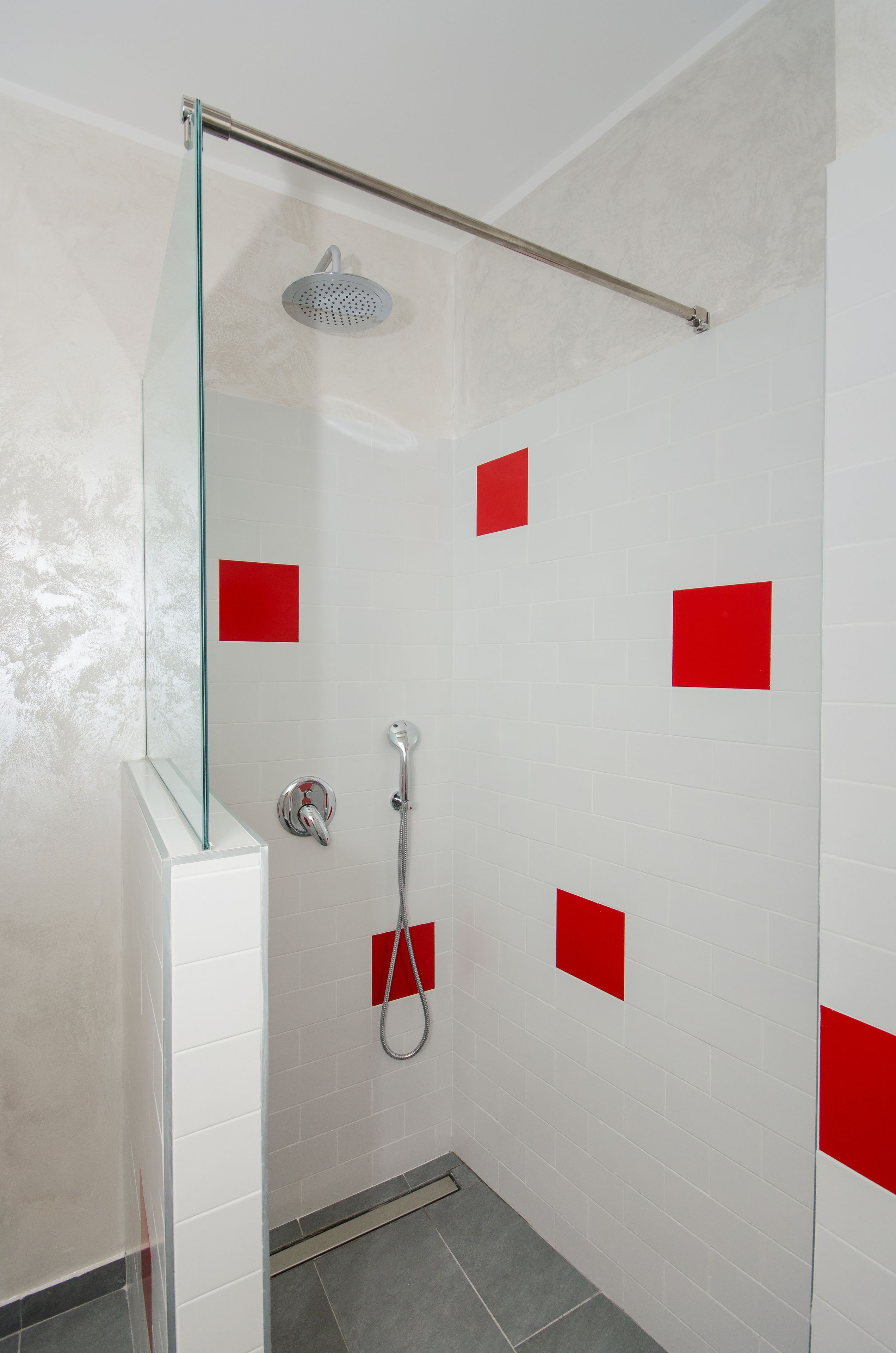 A shower with a glass door, a handheld showerhead, and red square tiles on the wall.