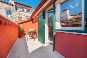 A narrow outdoor corridor with a red wall and a green door, leading to a room with a large window.
