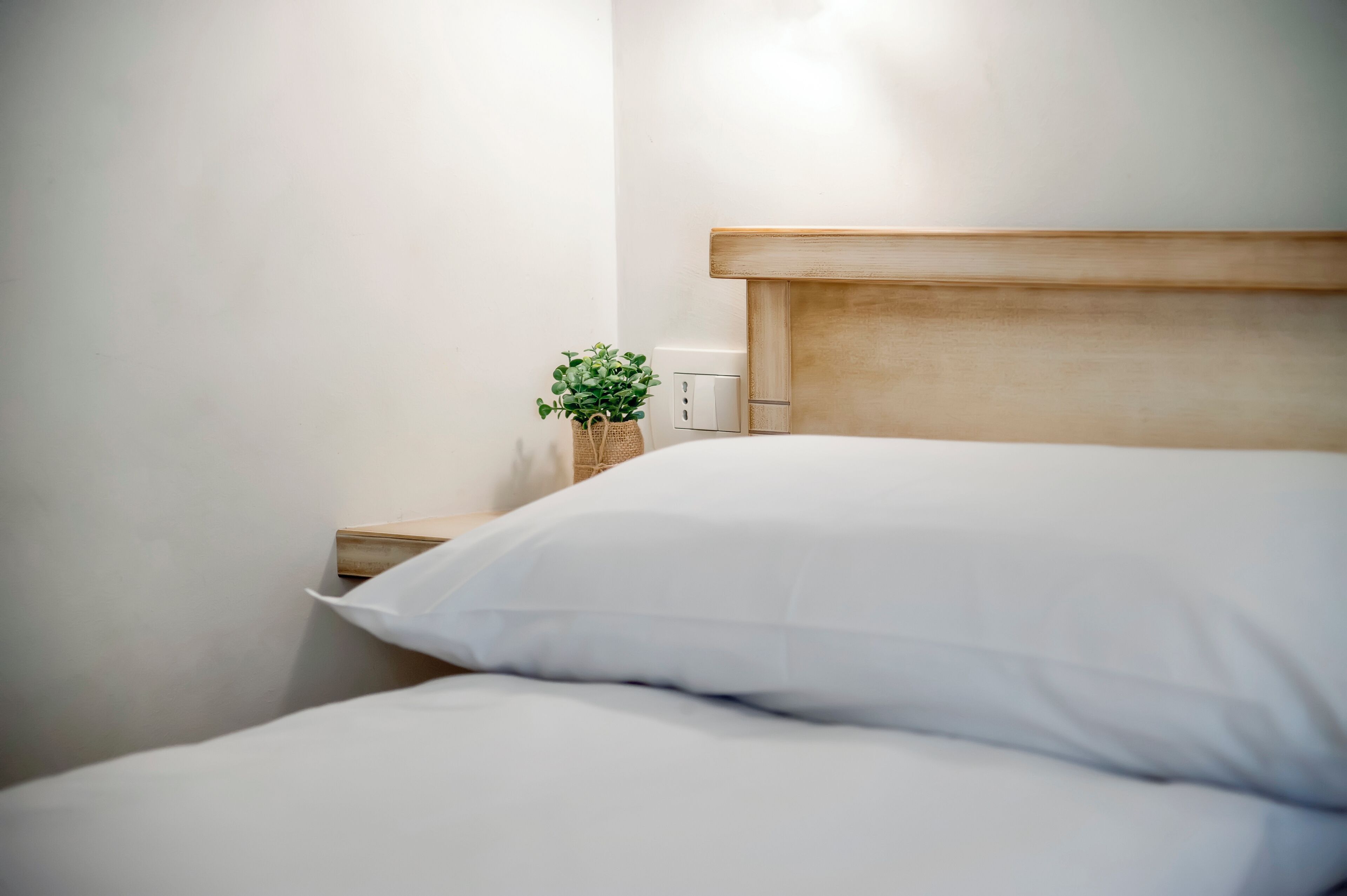 A neatly made bed with white linens and a wooden headboard.