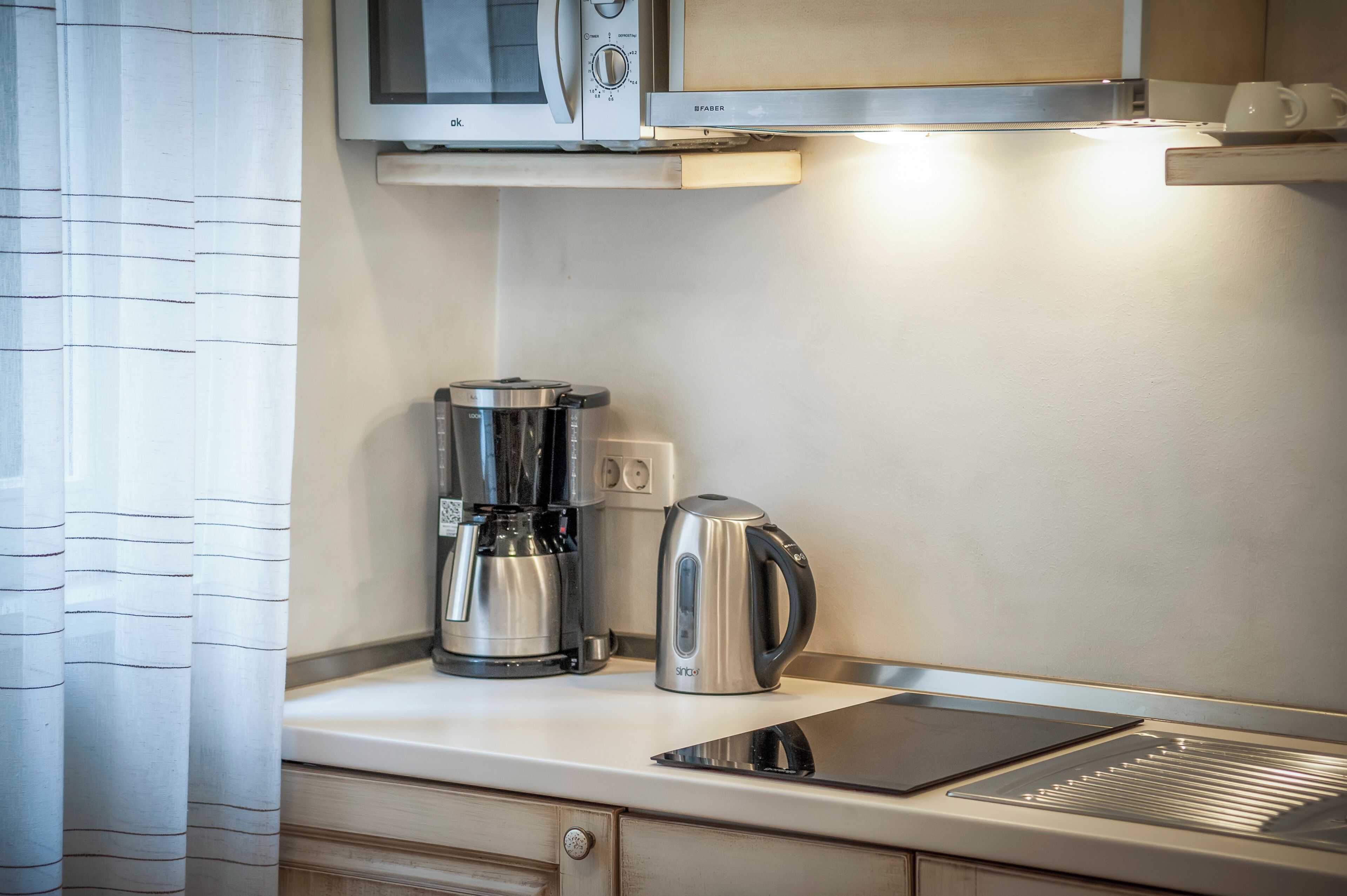 Una cucina con forno a microonde, macchina del caffè e bollitore sul piano di lavoro.