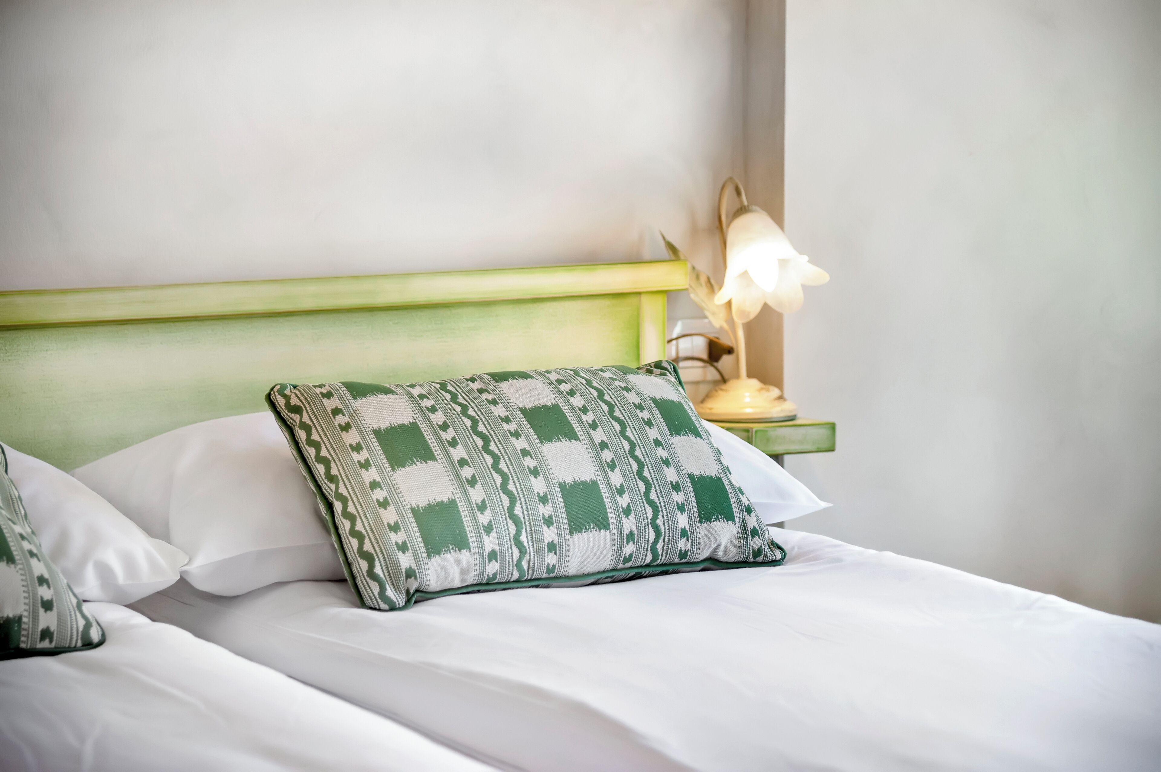 A neatly made bed with white linens and a green and white patterned pillow.