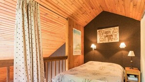 Ein Schlafzimmer mit Holzboden, einem Bett mit gemustertem Überwurf, zwei Wandlampen und einem kleinen Nachttisch.