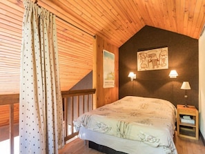 Ein Schlafzimmer mit Holzboden, einem Bett mit gemustertem Überwurf, zwei Wandlampen und einem kleinen Nachttisch.