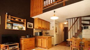 Ein gemütliches Wohnzimmer mit Fernseher, Holzmöbeln, einem Essbereich mit Tisch und Stühlen sowie einer Küche mit Holzausstattung und Geräten.
