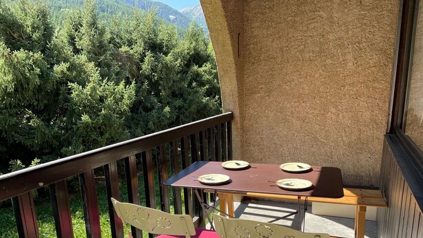 Ein Balkon mit Tisch und zwei Stühlen, mit Blick auf ein bewaldetes Gebiet.