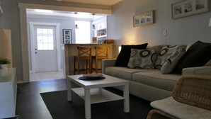Un salon avec un canapé, une table basse et un coin repas comprenant des chaises, et une cuisine en arrière-plan.