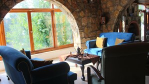 A cozy room with stone walls, a large arched window, and a fireplace.